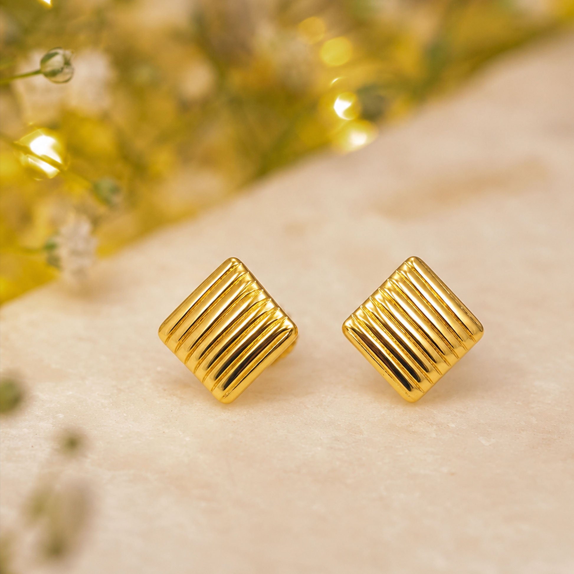 Close-up view of gold ribbed square stud earrings with polished finish