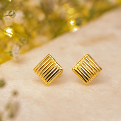 Close-up view of gold ribbed square stud earrings with polished finish